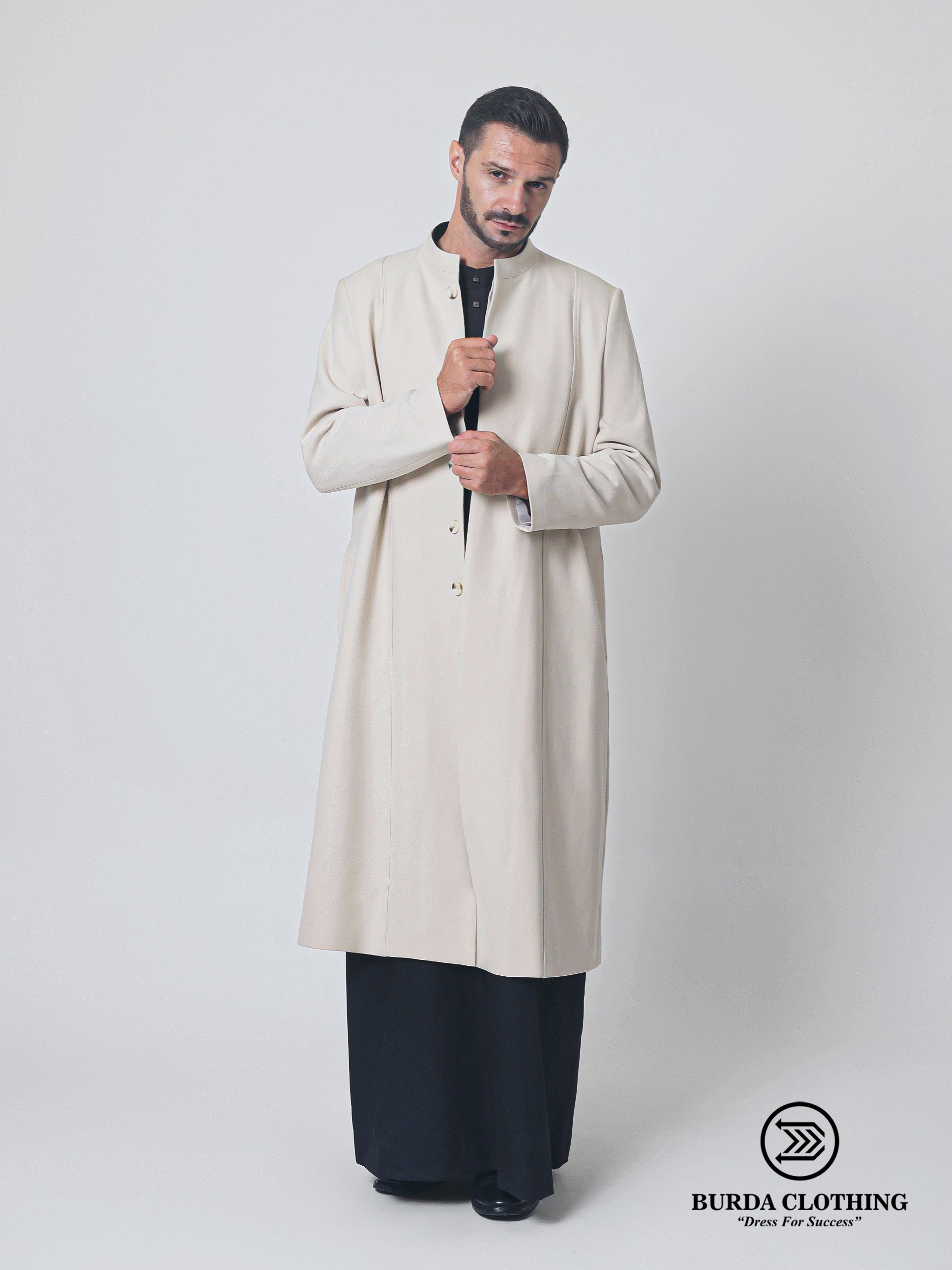 A man modeling a long-sleeved beige coat with a stand collar, paired with black wide-leg trousers, against a light gray studio background. The Burda Clothing brand logo is visible in the bottom right corner.