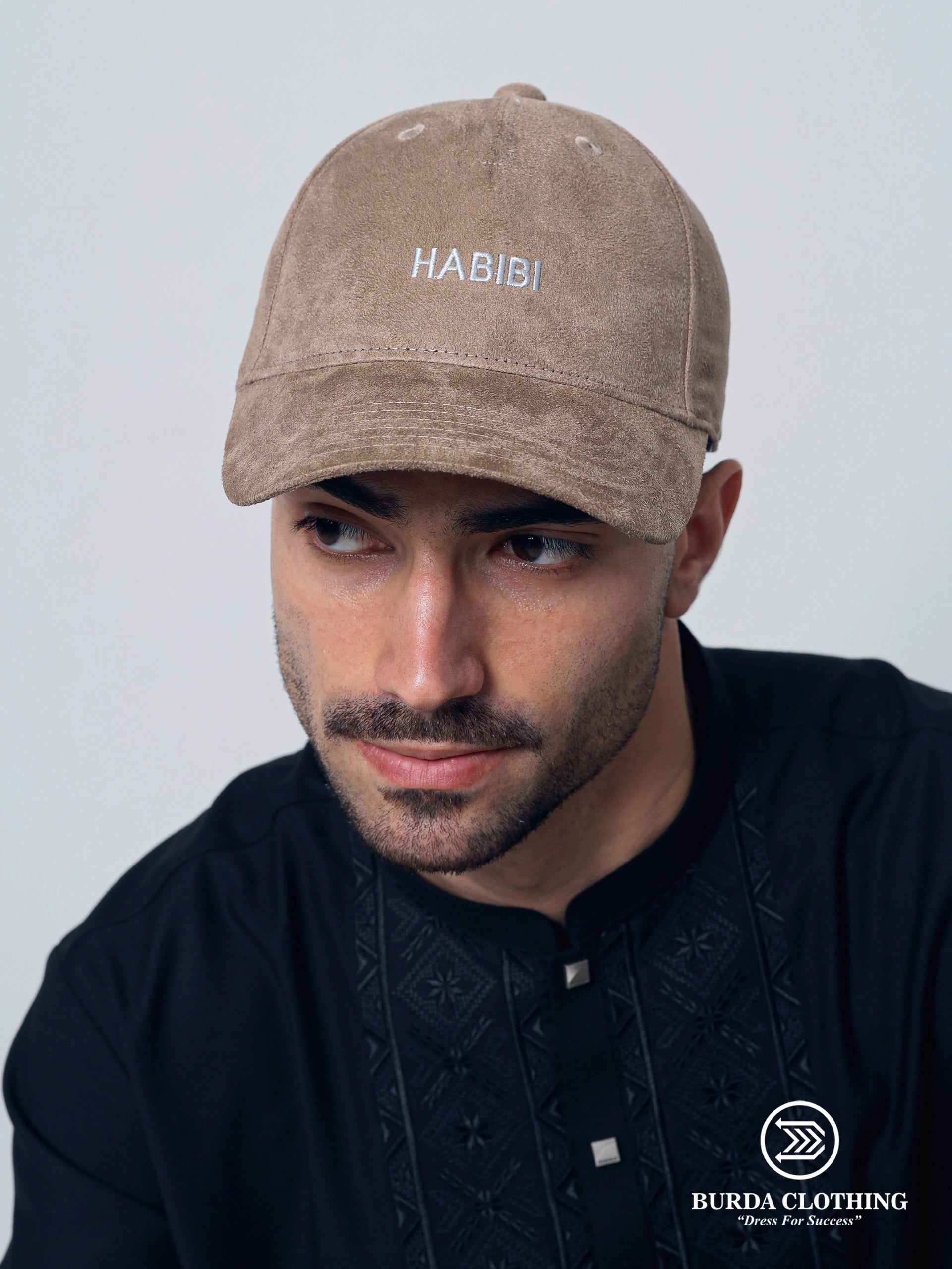 Man wearing a brown cap with 'HABIBI' text, against a plain background